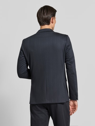 Männermodel trägt Slim Fit Sakko mit Pattentaschen Modell 'Gringo' von CG – CLUB of GENTS, feine Nadelstreifen, Rückenansicht, Ganzkörperansicht Rückansicht, Material-Mix mit Viskose-Anteil, Zweireiher, dunkel gehaltene Farben, glatte Textur.