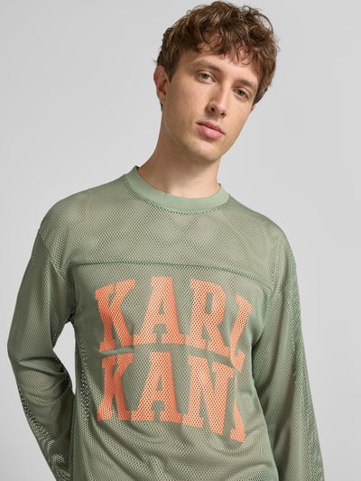 Männermodel trägt Longsleeve mit Label-Patch und Rundhalsausschnitt von KARL KANI, Logo-Print, Boxy-Fit, Nahaufnahme Oberkörper.