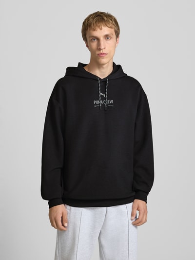 Männermodel trägt Hoodie mit Logo von PUMA PERFORMANCE in Schwarz, Relaxed Fit, Kapuze, Materialmix, Nahaufnahme Oberkörper.