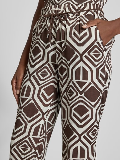 Frauenmodel trägt Stoffhose mit Bindegürtel Modell 'Pia' von TONI in Braun und Weiß mit geometrischen Formen, reine Viskose, Wide Fit, 7/8-Länge, Allover-Look, Nahaufnahme Oberkörper.