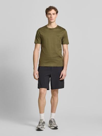 Męski model nosi Regular Fit T-Shirt aus reiner Baumwolle Modell 'PS Spirit 70 Grx' od BOSS Green X PORSCHE, kolor khaki, fason krój regular fit, aplikacja z logo, dekolt okrągły, krótki rękaw, elastyczna bawełna, całkowity widok z przodu.