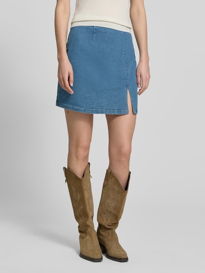 Frauenmodel trägt eng anliegenden Jeansrock aus Baumwoll-Mix Modell 'NELLY' von Vero Moda in Denim-Optik, Mini-Länge, Regular-Fit, gerade Textur, Bundabschluss mit Frontschlitz, verdeckter Reißverschluss, Ganzkörperansicht von vorne.