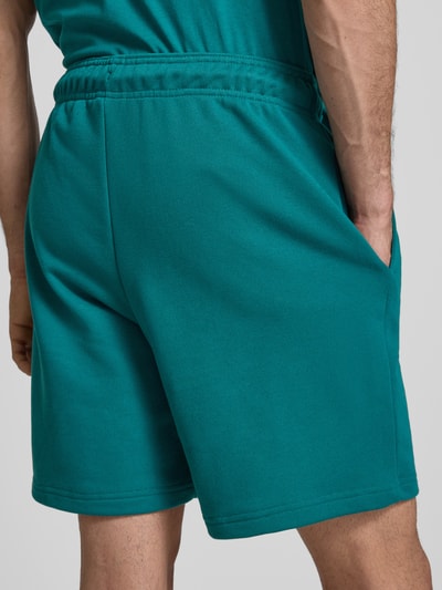 Männermodel trägt Sweatshorts mit Logo und elastischem Bund von CHAMPION in Türkis, Baumwoll-Mix, Regular Fit, Ganzkörperansicht Rückansicht.
