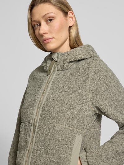 Frauenmodel trägt Regular Fit Jacke mit Kunstfellbesatz von camel active in Beige mit Stehkragen, Kapuze, Zweiwege-Reißverschluss, Eingrifftaschen sowie elastischen Ärmelabschlüssen, Nahaufnahme Oberkörper.