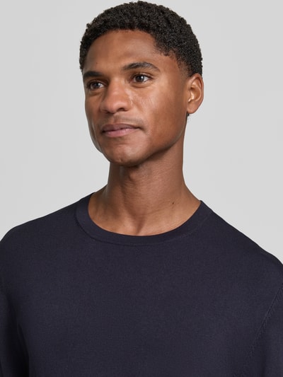Männermodel trägt Strickpullover mit geripptem Rundhalsausschnitt von MCNEAL in Dunkelblau, leichte Struktur, Nahaufnahme Oberkörper, taillierte Passform, gerippte Abschlüsse, leicht überschnittene Schultern.