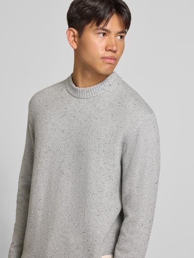Männermodel trägt Regular Fit Strickpullover mit Rundhalsausschnitt von JACK & JONES in hellgrau meliertem Baumwoll-Mix, Nahaufnahme Oberkörper, Logo-Patch sichtbar.