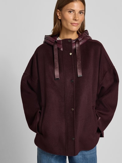 Frauenmodel trägt Jacke mit Kapuze von COMMA in dunklem Bordeaux, lockere Passform, seitliche Taschen, Knopfleiste, Nahaufnahme Oberkörper.