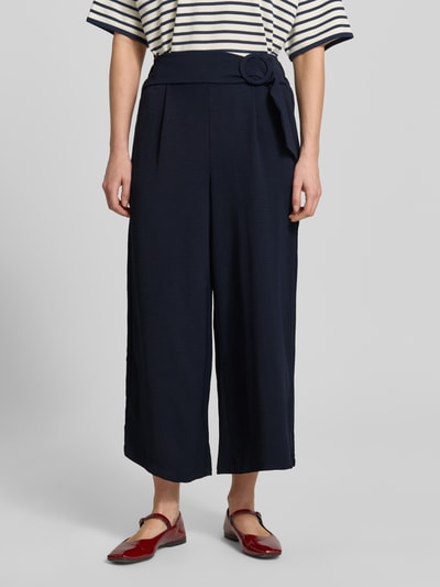 Vrouwenmodel draagt Wide Fit Stoffhose mit Bundfalten van Zero, donkerblauw met bandplooien, siergesp, verkorte pasvorm, comfortband, bandwijdte maat 36: 34 cm, binnenbeenlengte: 61 cm, wide fit, cropped design, textuur fijn, detailopname vooraan.