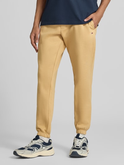 Männermodel trägt Slim Fit Sweathose aus Baumwoll-Mix von Tommy Jeans in Beige, glatte Struktur, Ganzkörperansicht von vorne, Herren Sweathose.
