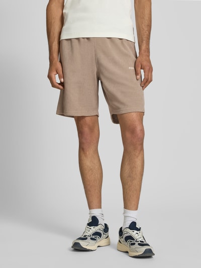 Mannenmodel draagt Relaxed Fit Shorts met structuurpatroon model 'Lagos' van Pegador, elastische materiaalmix, zandkleur, elastische band, bandwijdte maat M 38 cm, binnenbeenlengte maat M 21 cm, short, ganzekörperaanzicht van voren.