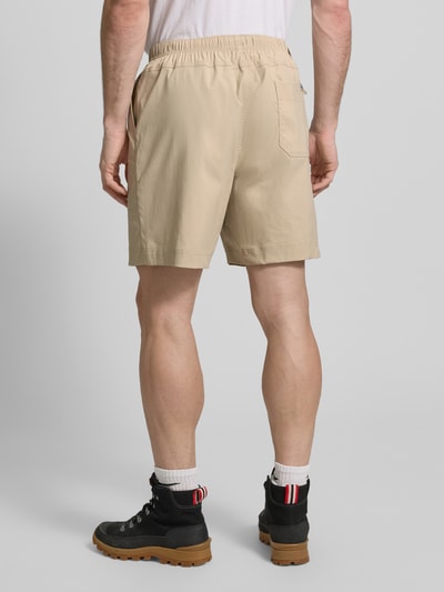 Männermodel trägt Regular Fit Shorts mit Logo-Patch Modell 'Landroamer' von COLUMBIA in Beige mit elastischem Bund und aufgesetzten Taschen, Ganzkörperansicht Rückansicht.