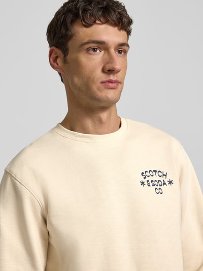 Männermodel draagt Sweatshirt met Label-Print van Scotch & Soda, crème kleur, ronde hals, regular fit, Nahaufnahme bovenlichaam.