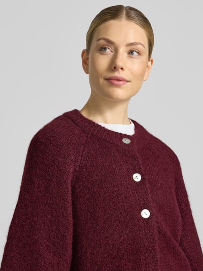 Vrouwenmodel draagt Relaxed Fit Cardigan met wol van FREE/QUENT, elastische materiaalmix, model 'Lulu', tricotlook, 3/4-mouw, ruglengte maat S 59 cm, mouwlengte maat S 48 cm, bordeauxrode kleur, knoopsluiting met witte knopen, detailopname bovenlichaam.