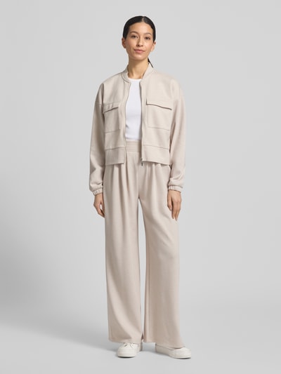 Modelka kobieca nosi Piqué Blouson Jacke mit Taschen od Christian Berg Woman, kremowy materiał miks z bawełną, prosty krój, piqué, kieszenie z patkami, stójka, zamek, elastyczne mankiety, obniżone ramiona, widok całej sylwetki z przodu.