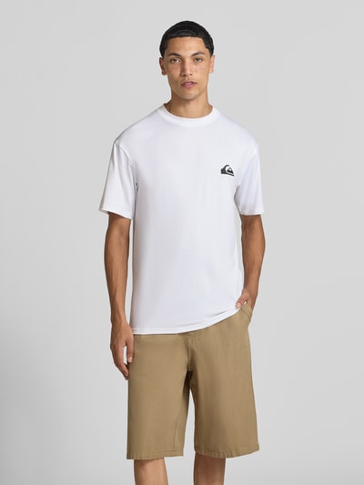 Männermodel trägt T-Shirt mit Rundhalsausschnitt und Logo von Quiksilver in wit, regular fit Materiaalmix met stretch, ruglengte maat M 75 cm, ganzlichaamsvoorzijde