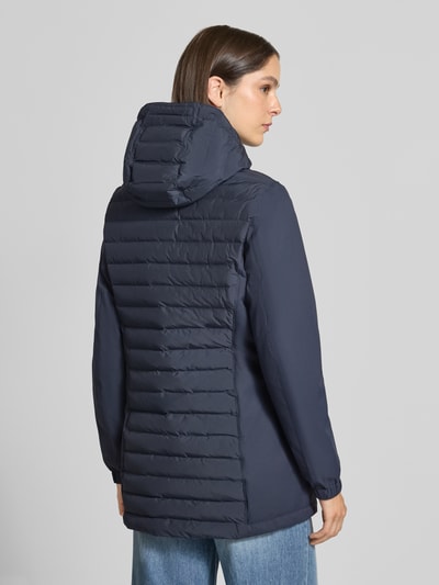 Modelka nosi płaszcz pikowany 'Steppmantel mit Zweiwege-Reißverschluss' od camel active, granatowy kolor, gładka tekstura, wpuszczane kieszenie, kaptur z tunelem, zamek błyskawiczny dwustronny z zabezpieczeniem, elastyczne zakończenia rękawów, długość tyłu 77 cm w rozmiarze 36, szerokość ramion 42 cm, szerokość w klatce piersiowej 52 cm, długość rękawów 66 cm, widok całej sylwetki z tyłu.