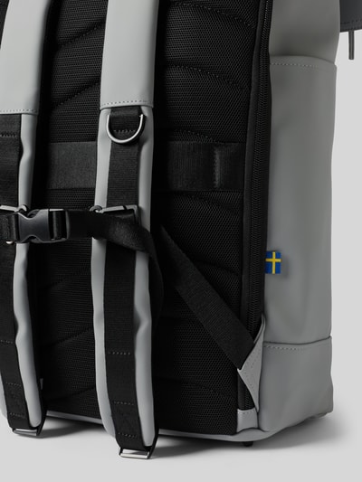 Produktfoto, grauer und schwarzer Rucksack mit Logo-Detail Modell 'Spläsh Rolltop' von GASTON LUGA, verstellbare Schulterriemen, robuste Textur und gestepptes Rückenteil, schwedische Flagge sichtbar, Hauptfach mit Reißverschluss, Maße: 42x48x14 cm, Länge Schulterriemen 88 cm.