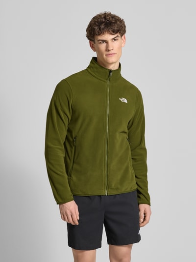 Männermodel trägt Fleecejacke mit Stehkragen Modell 'GLACIER' von The North Face in Olivgrün, gerader Schnitt, Ganzkörperansicht von vorne.