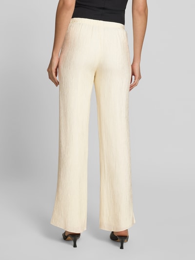Frauenmodel trägt Stoffhose aus Viskose-Mix von Anine Bing in Beige mit Crinkle-Optik, lockerer Passform und elastischem Bund, Ganzkörperansicht Rückansicht.