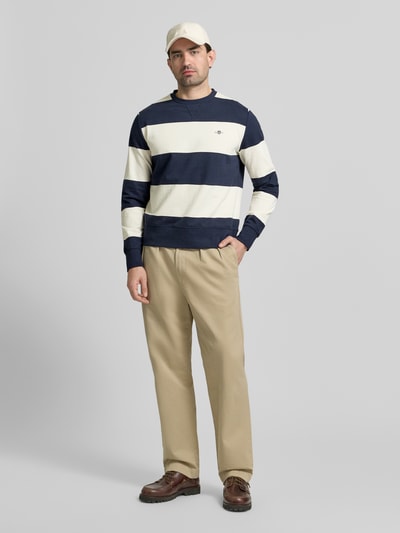 Männermodel trägt Regular Fit Pullover in Strick-Optik von Gant in Dunkelblau und Creme, Stehkragen, Logo-Stitching, Ganzkörperansicht von vorne.