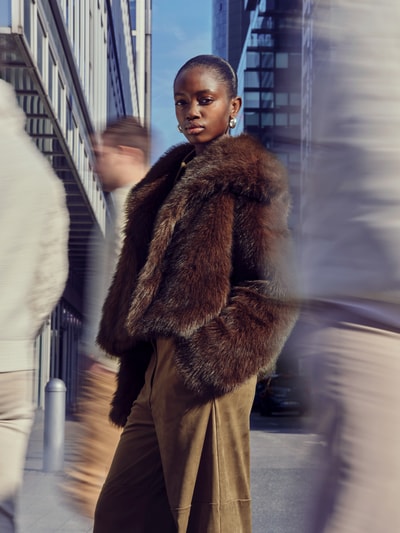 Kobieta modelka nosi Relaxed Fit Webpelzjacke mit Hakenverschluss Modell 'DAWN LIFE' od Only, sztuczne futro, jednokolorowy, wykładany kołnierz, wpuszczane kieszenie, długi rękaw, brązowy, efekt: jednolity kolor, materiał: sztuczne futro, całkowita długość tyłu 51 cm w rozmiarze S, szerokość klatki piersiowej 56 cm, szerokość ramion 42 cm, długość rękawa 60 cm, zdjęcie całej sylwetki z przodu.
