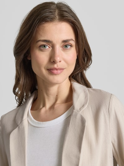 Vrouwenmodel draagt Loose Fit Kurzblazer aus Viskose-Leinen-Mix Modell 'JESMILO' van Vero Moda in effen beige flammengaren stof, reverskraag, zonder sluiting, 3/4-mouw met vaste omslag, fake paspelzakken, materiaal glad met lichte textuur, close-up van het bovenlichaam.