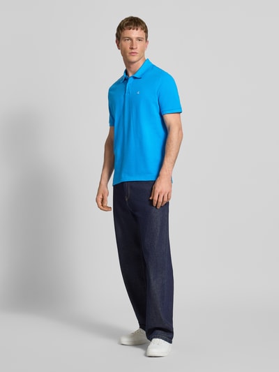 Männermodel trägt Straight Fit Poloshirt mit Label-Stitching von Calvin Klein Jeans in Blau aus reiner Baumwolle, Ganzkörperansicht von vorne.
