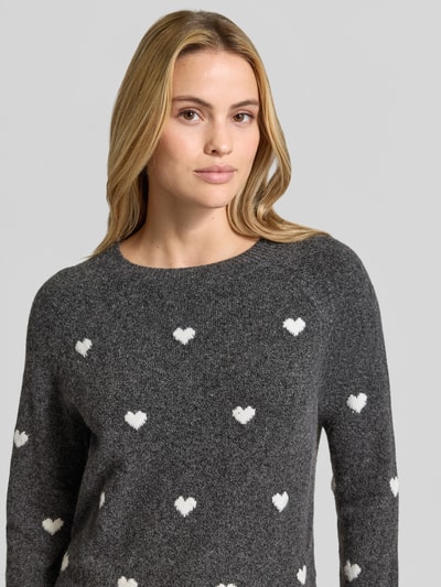 Frauenmodel trägt Regular Fit Pullover mit Rundhalsausschnitt Modell 'DOFFY' von VERO MODA in Dunkelgrau mit weißen Herzen, Nahaufnahme Oberkörper. Damen Pullover von VERO MODA.