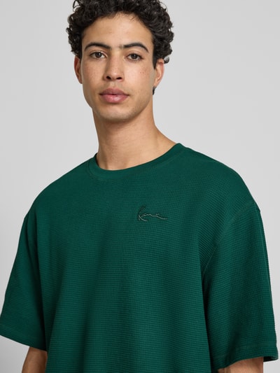 Männermodel trägt Oversized T-Shirt mit Logo-Stitching von KARL KANI in Dunkelgrün, Reine Baumwolle, Rundhalsausschnitt, Oversized-Fit, Nahaufnahme Oberkörper. Rückenlänge bei Größe M: 73 cm.