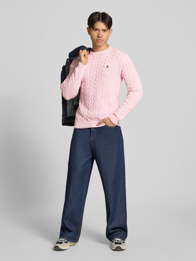Männermodel trägt Strickpullover mit Zopfmuster und Logo-Stitching von REVIEW in Rosa aus Baumwoll-Mix, Modern Fit, Ganzkörperansicht von vorne.