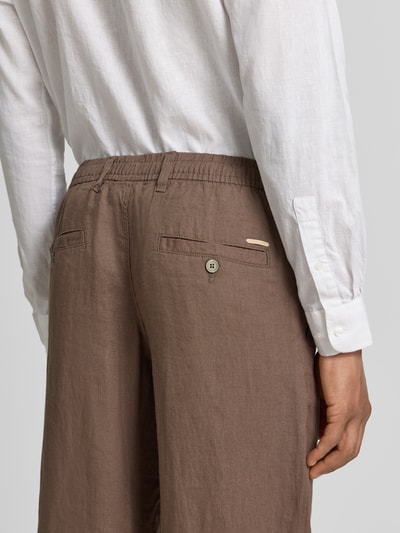 Männermodel trägt Leinenhose mit Eingrifftaschen Modell 'KARL LAWRENCE' von Jack & Jones Premium, braun, lockere Textur, Ganzkörperansicht Rückansicht. Herren Leinenhose aus Reinem Leinen mit Straight Fit, elastischem Bund, Knopf-Reißverschluss, französischen Eingrifftaschen, Gesäßleistentaschen, Bundweite 42 cm, Innenbeinlänge 75 cm bei Größe M.