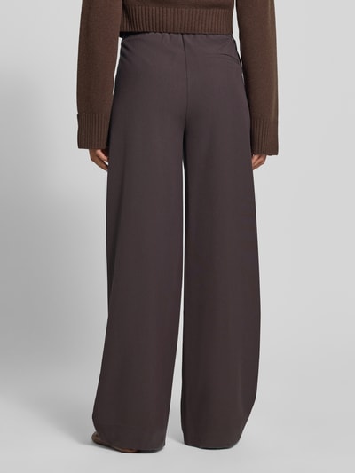 Frauenmodel trägt Wide Fit Sweatpants mit Viskose-Anteil von MYON in Dunkelbraun, elastischer Bund, glatte Oberfläche, Ganzkörperansicht Rückansicht.