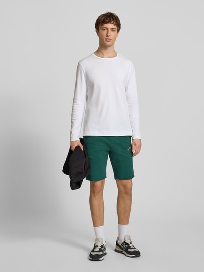 Männermodel trägt grüne Shorts mit Logo-Print Modell 'GORDON' von Jack & Jones aus Baumwoll-Mix, Relaxed-Fit, elastischer Bund mit Kordelzug, Ganzkörperansicht von vorne.