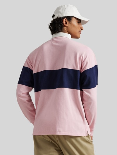 Männermodel trägt Regular Fit Poloshirt aus reiner Baumwolle von Polo Ralph Lauren in Rosa mit navyfarbenem Streifen, Unifarbe, Piqué-Struktur, Ganzkörperansicht Rückansicht.