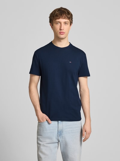 Männermodel trägt Regular Fit T-Shirt aus reiner Baumwolle von Tommy Jeans, unifarben, Logo-Stitching, Nahaufnahme Oberkörper.