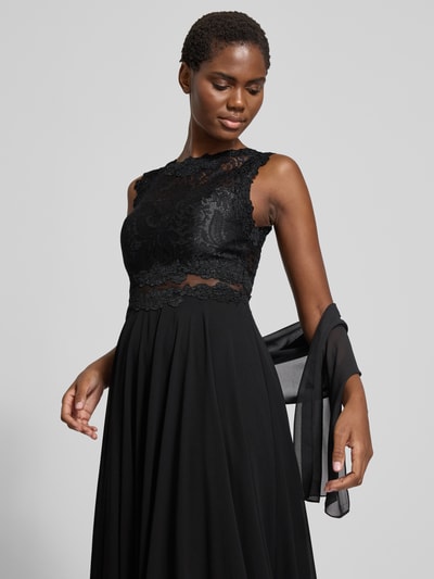 Frauenmodel trägt Abendkleid mit Spitze und Rundhalsausschnitt von Mascara in Schwarz, A-Linie, Maxikleid, Ganzkörperansicht von vorne. Rückenlänge bei Größe 36: 153 cm, Brustweite bei Größe 36: 33 cm.