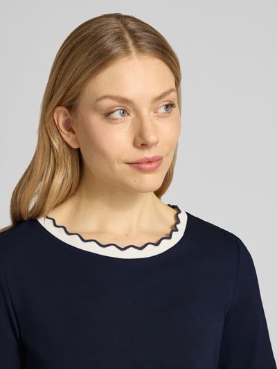 Modelka kobieca nosi T-Shirt mit Rundhalsausschnitt und Wellensaum od More & More, ciemnogranatowy, bawełna z elastanem, krój regular fit, okrągły dekolt, falisty brzeg, długość tyłu w rozmiarze 36: 57 cm, zbliżenie na górną część ciała