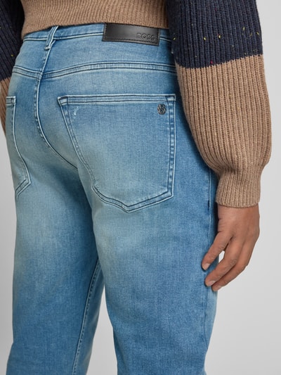 Männermodel trägt Slim Fit Jeans aus Baumwoll-Mix Modell 'DELAWARE' von BOSS Orange, Denim-Optik, Label-Patch, Detailaufnahme Rückansicht.