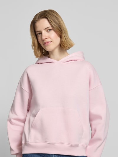 Frauenmodel trägt Regular Fit Hoodie mit Känguru-Tasche Modell 'Iconic' von Gina Tricot, Baumwoll-Mix, elastische Abschlüsse, hellrosa, Ganzkörperansicht von vorne.