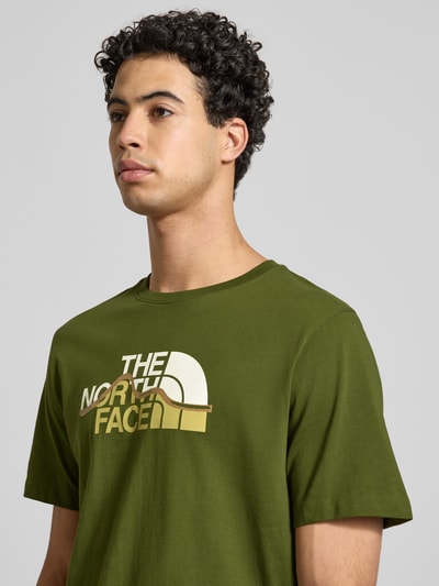 Männermodel trägt Regular Fit T-Shirt aus reiner Baumwolle Modell 'MOUNTAIN LINE' von The North Face, Olivgrün, Label-Print, Nahaufnahme Oberkörper. Herren T-Shirt, Rundhalsausschnitt, Rückenlänge bei Größe M: 70 cm.