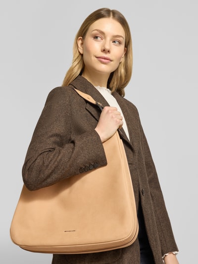 Kobiece model prezentuje Hobo Bag mit Label-Detail Modell 'NOLITA' od MICHAEL Michael Kors w kolorze beżowym, faktura gładka, szerokość w rozmiarze 1: 40 cm, długość 42 cm, głębokość 10 cm, długość paska 36 cm, zbliżenie górnej części ciała z przodu.