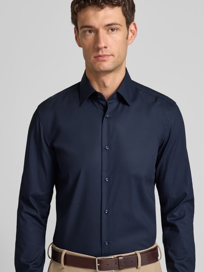 Męski model nosi Slim Fit Businesshemd aus Popeline mit Stretch-Anteil od BOSS, ciemnogranatowy, guzikami, bawełna-elastan, widok z przodu, z kontekstem: krój slim fit, kołnierz kent, pełny plisk, sportowe mankiety, zaokrąglony dół, easycare, długość pleców 76 cm, szerokość ramion 47 cm, długość rękawa 67 cm. Ganzkörperansicht von vorne.