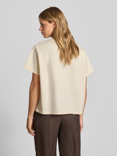 Frauenmodel trägt T-Shirt mit Logo-Stitching Modell 'Ella' von OH APRIL in Beige, reine Baumwolle, Boxy Fit, Rückenansicht, Ganzkörperansicht.