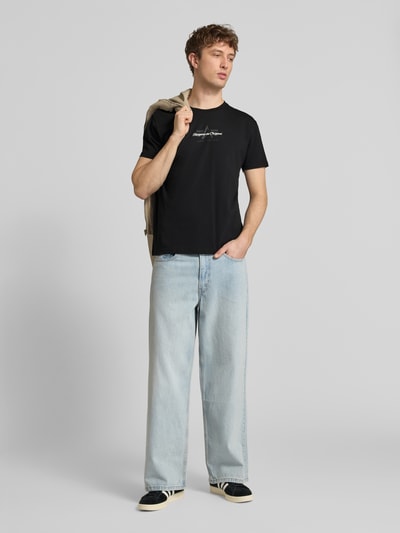 Męski model nosi T-Shirt mit Label-Detail Modell 'Foam' od Alpha Industries, czarny kolor, krój regular fit, czysta bawełna, przód, zdjęcie całej sylwetki.