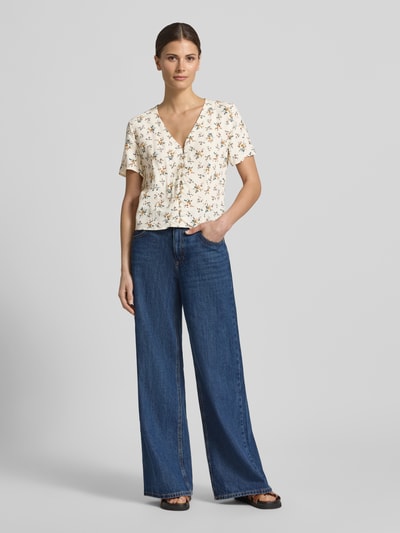 Kobiece modelka nosi Slim Fit Bluse aus reiner Viskose von Jake*s Casual, kremowa bluzka z wiskozy, krój slim fit, kwiatowy nadruk na całej powierzchni, dekolt w serek, z krótkim rękawem i listwą guzikową, długość tyłu 50 cm, długość rękawów 20 cm, Ganzkörperansicht von vorne.