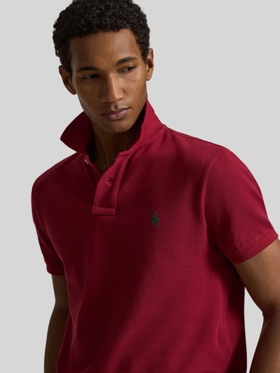 Mannelijk model draagt Regular Fit Poloshirt uit zuivere katoen van Polo Ralph Lauren in effen rood, piquéstructuur, logo-detail, close-up bovenlichaam.
