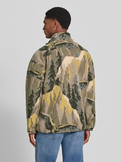 Männermodel trägt sweter z polaru Fleecepullover mit Label-Patch Modell 'HELVETIA' von Columbia w odcieniach zieleni, beżu i żółci, z motywem krajobrazu, prosty krój, stójka, długość tyłu w rozmiarze M: 73 cm, długość rękawów w rozmiarze M: 60 cm, Ganzkörperansicht Rückansicht