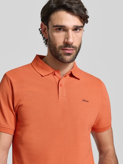 Männermodel trägt Regular Fit Poloshirt aus reiner Baumwolle von s.Oliver RED LABEL in Orange, Piqué-Struktur, Label Stitching, Nahaufnahme Oberkörper.