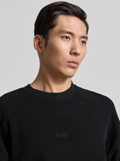 Männermodel trägt Regular Fit Sweatshirt aus reiner Baumwolle Modell 'DAFFLYN' von HUGO in Schwarz mit Strukturmuster, Nahaufnahme Oberkörper.
