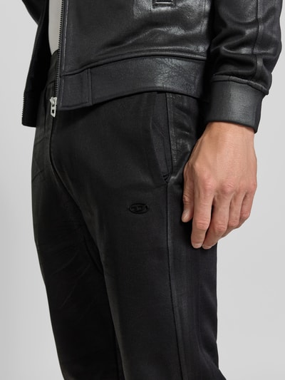 Männermodel trägt Flared Fit Hose aus Baumwoll-Mix von Diesel in schwarzer Leder-Optik mit Gesäßtasche und elastischem Bund, Nahaufnahme Oberkörper.
